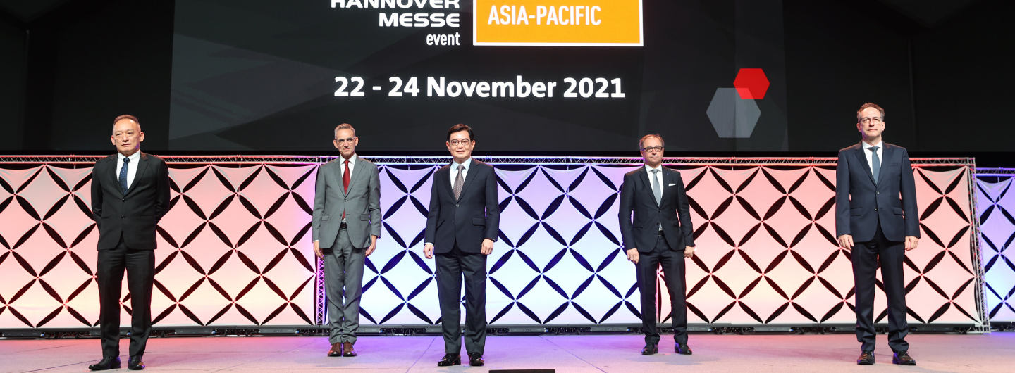 Five people in suits stand on a stage in front of "Hannover Messe Asia-Pacific" event signage.